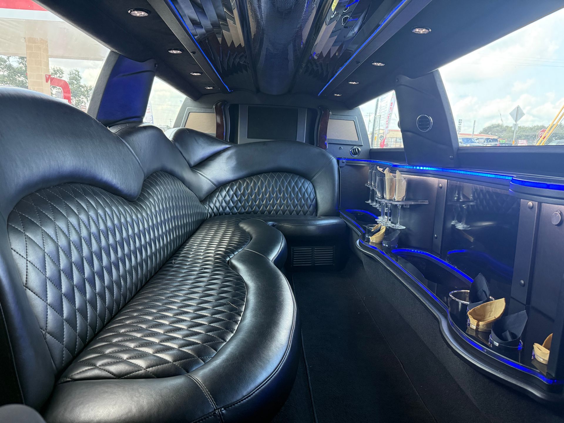 Interior of a limousine with black leather seats, a bar, and blue accent lights.