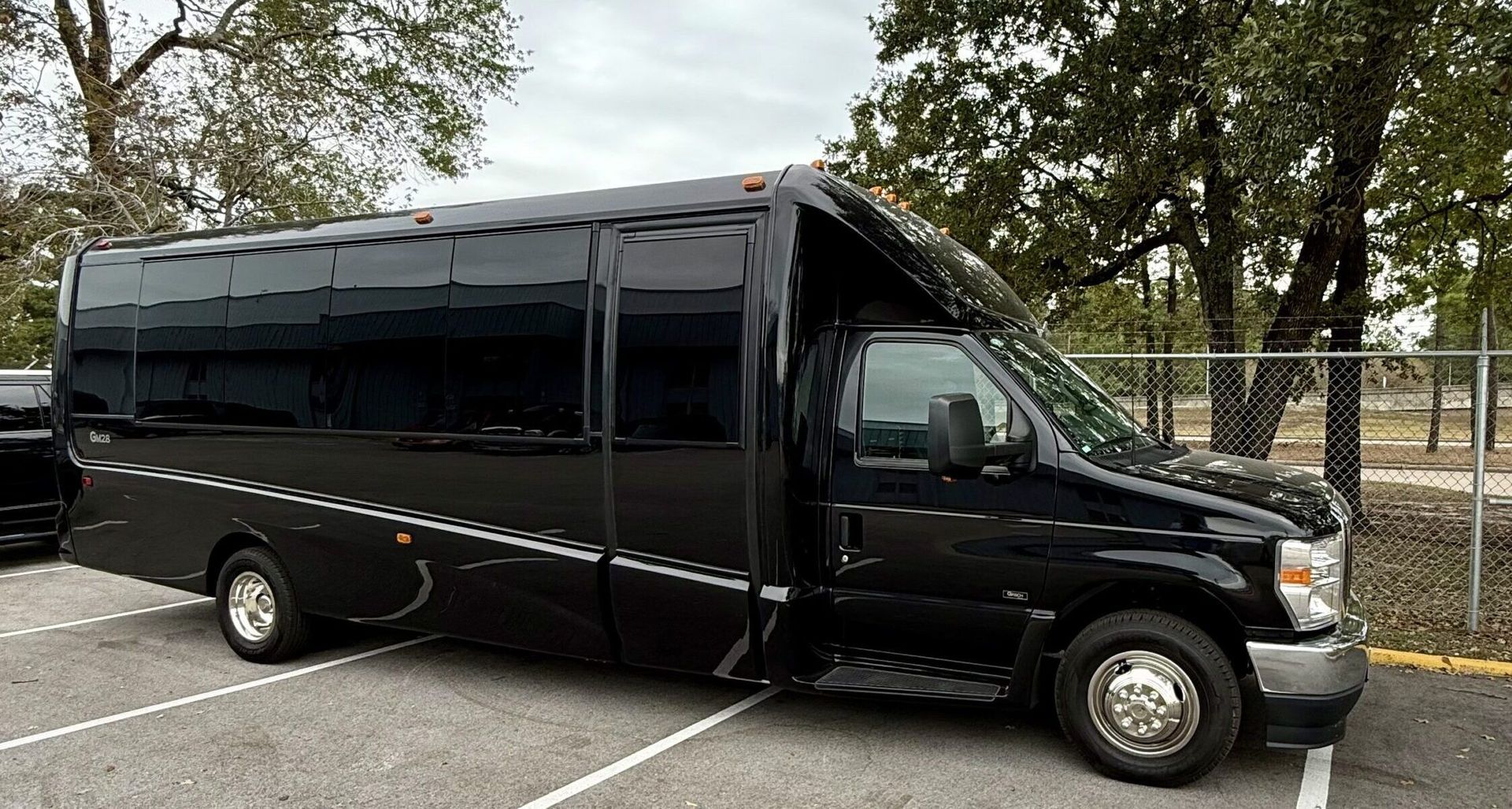 A black van is parked in a parking lot next to a fence.