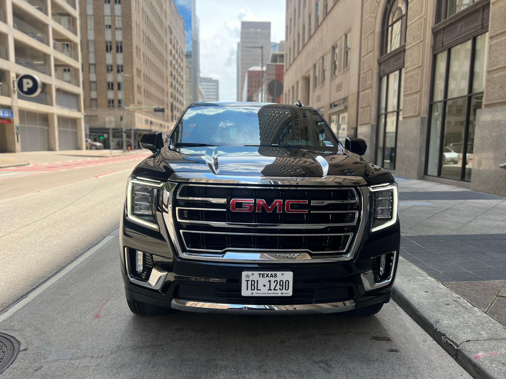 Black GMC Yukon SUV parked on a city street, Texas license plate. Buildings in background.