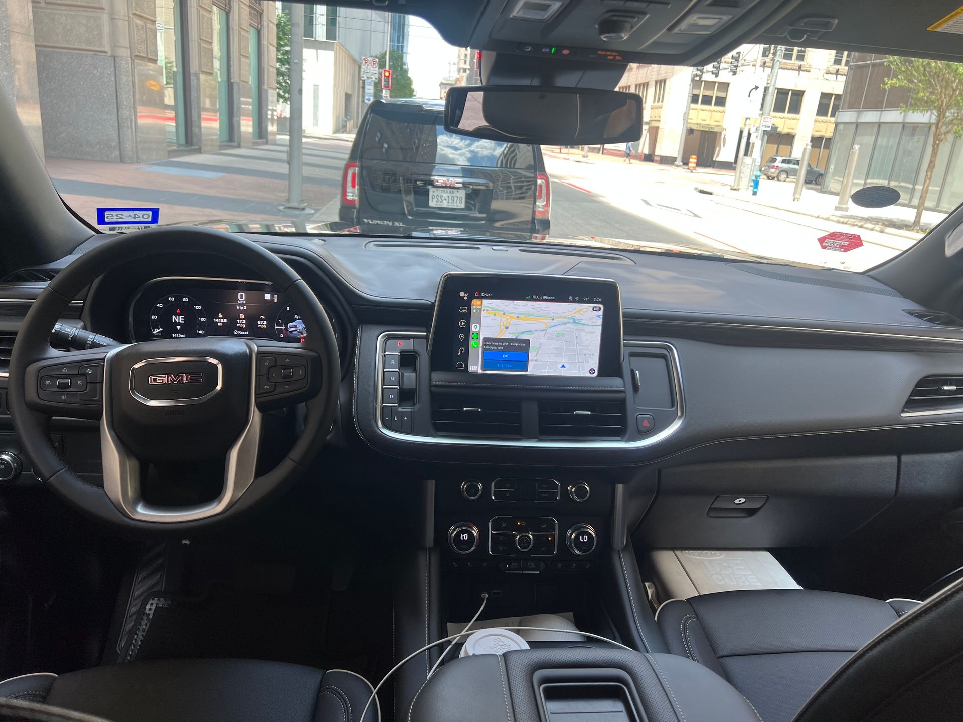 Interior view of a GMC Yukon. Dashboard with navigation screen, steering wheel, and a view of a city street.