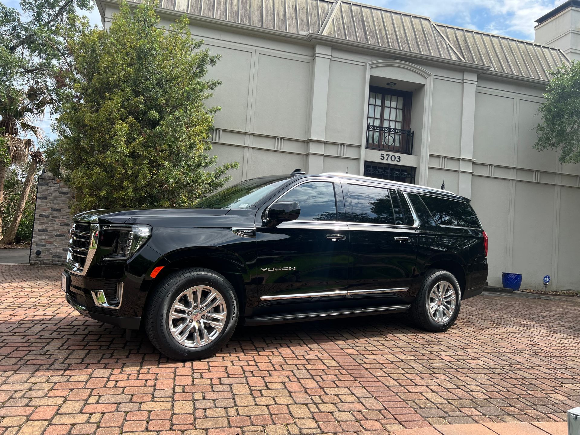 Black SUV parked on brick driveway in front of a light-colored building.