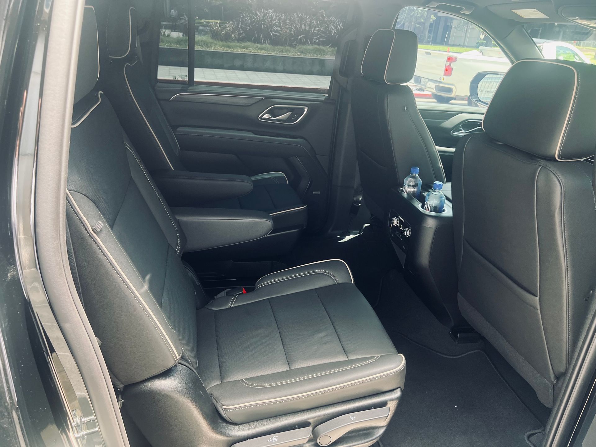 Black SUV interior with leather seats, white stitching, and a bottle of water in the center.