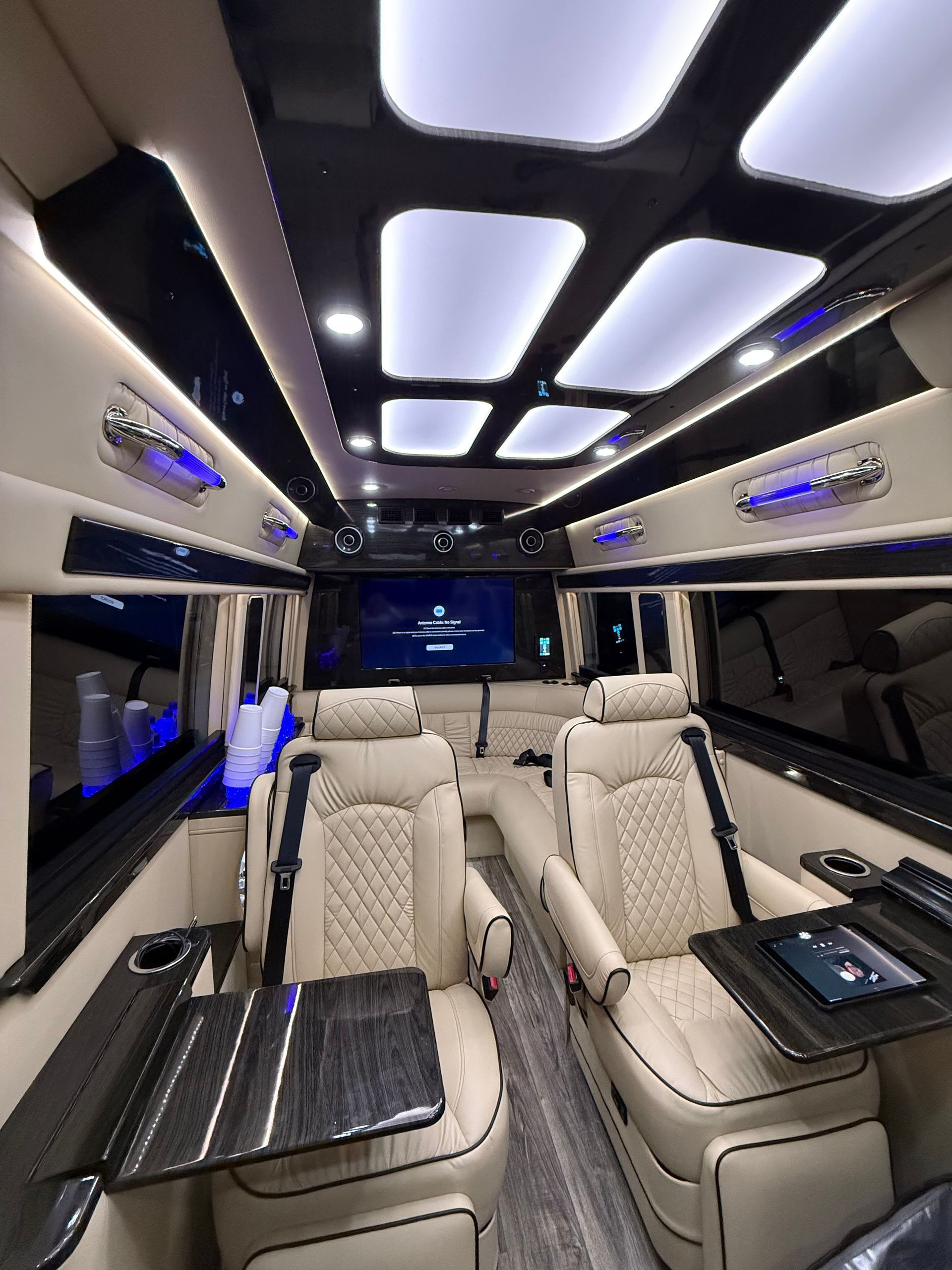 Luxurious van interior with cream leather seats, wood tables, and LED lighting.