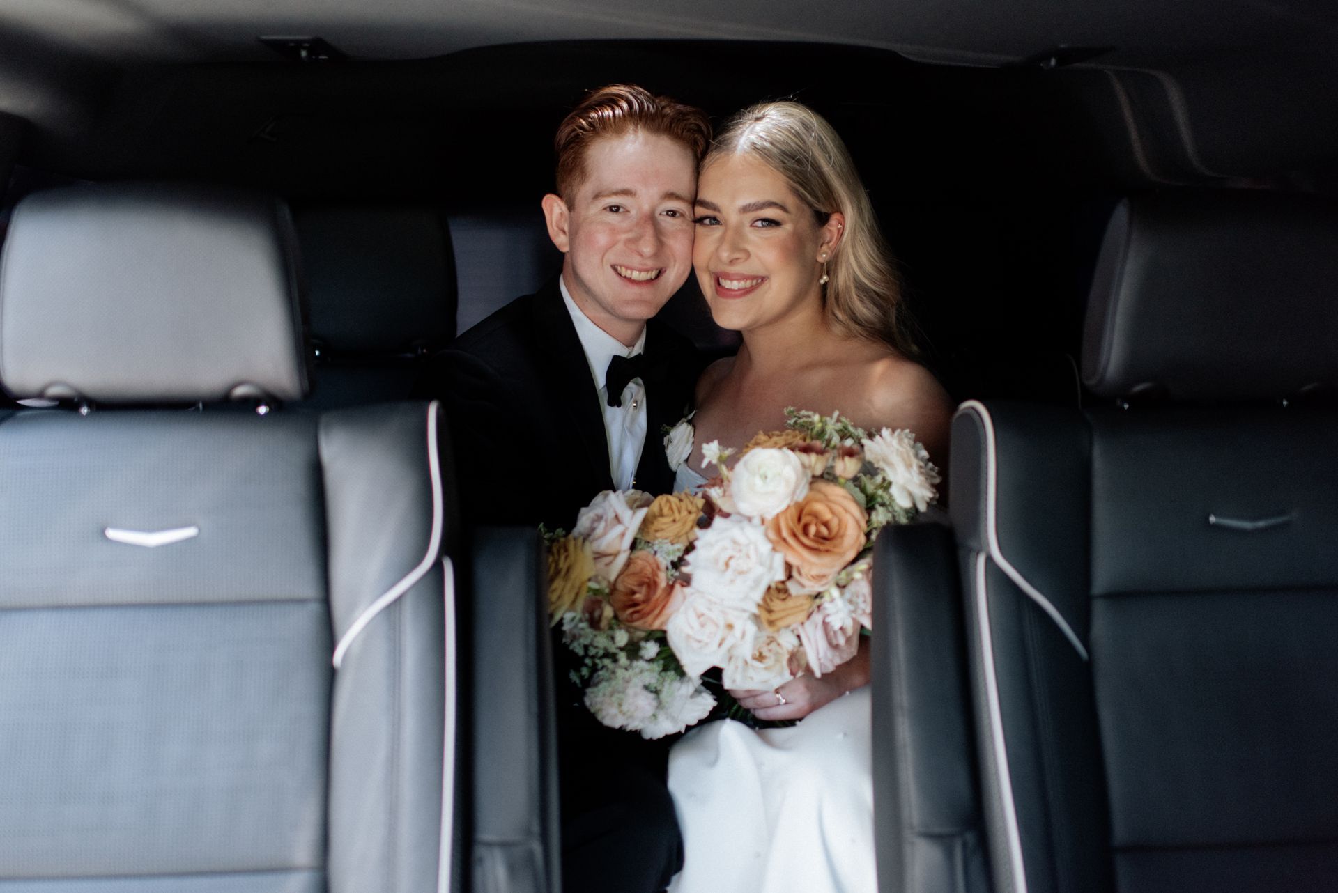A bride and groom are sitting in the back seat of a car