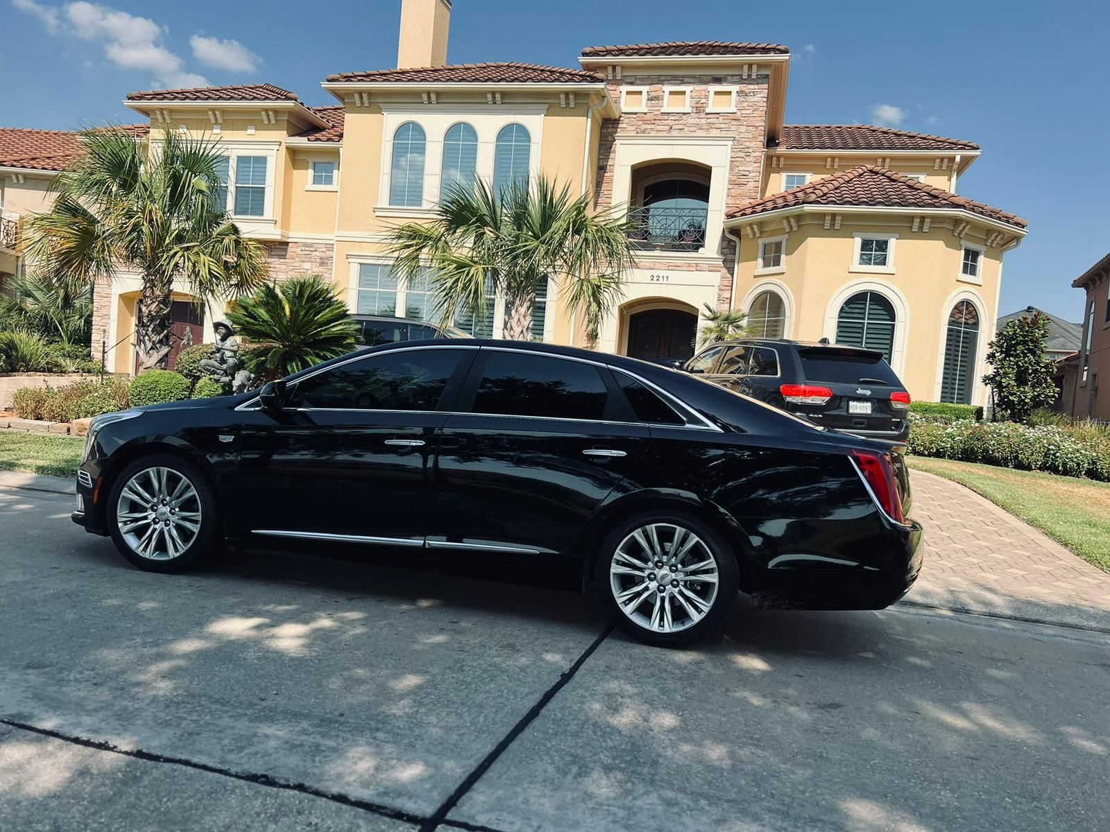 A black car is parked in front of a large yellow house.