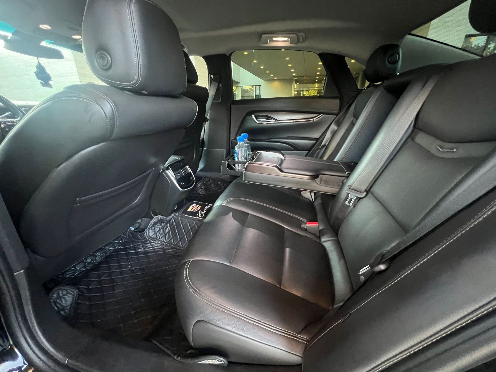 The back seat of a car with a bottle of water on the arm rest.