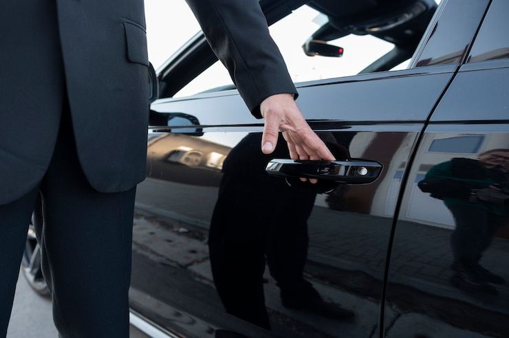 Your chauffeur awaits in front of a pristine luxury vehicle, 