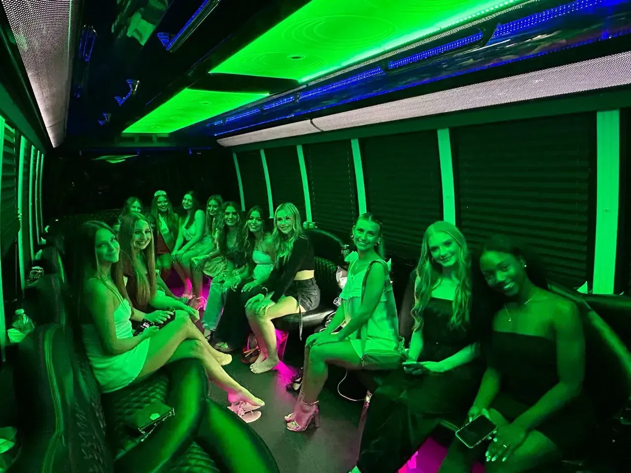 A group of women are sitting in a limousine with green lights on the ceiling.