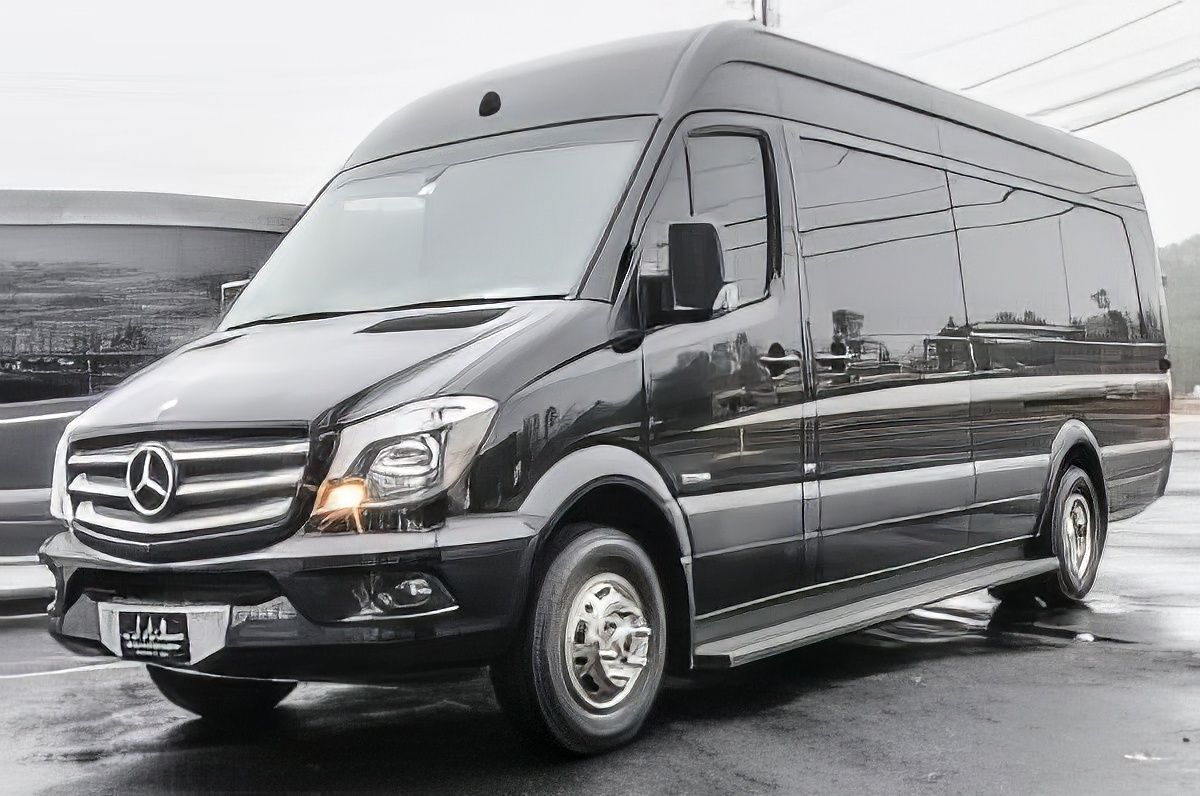 Black Mercedes Sprinter van parked on wet pavement. Side door step is visible.