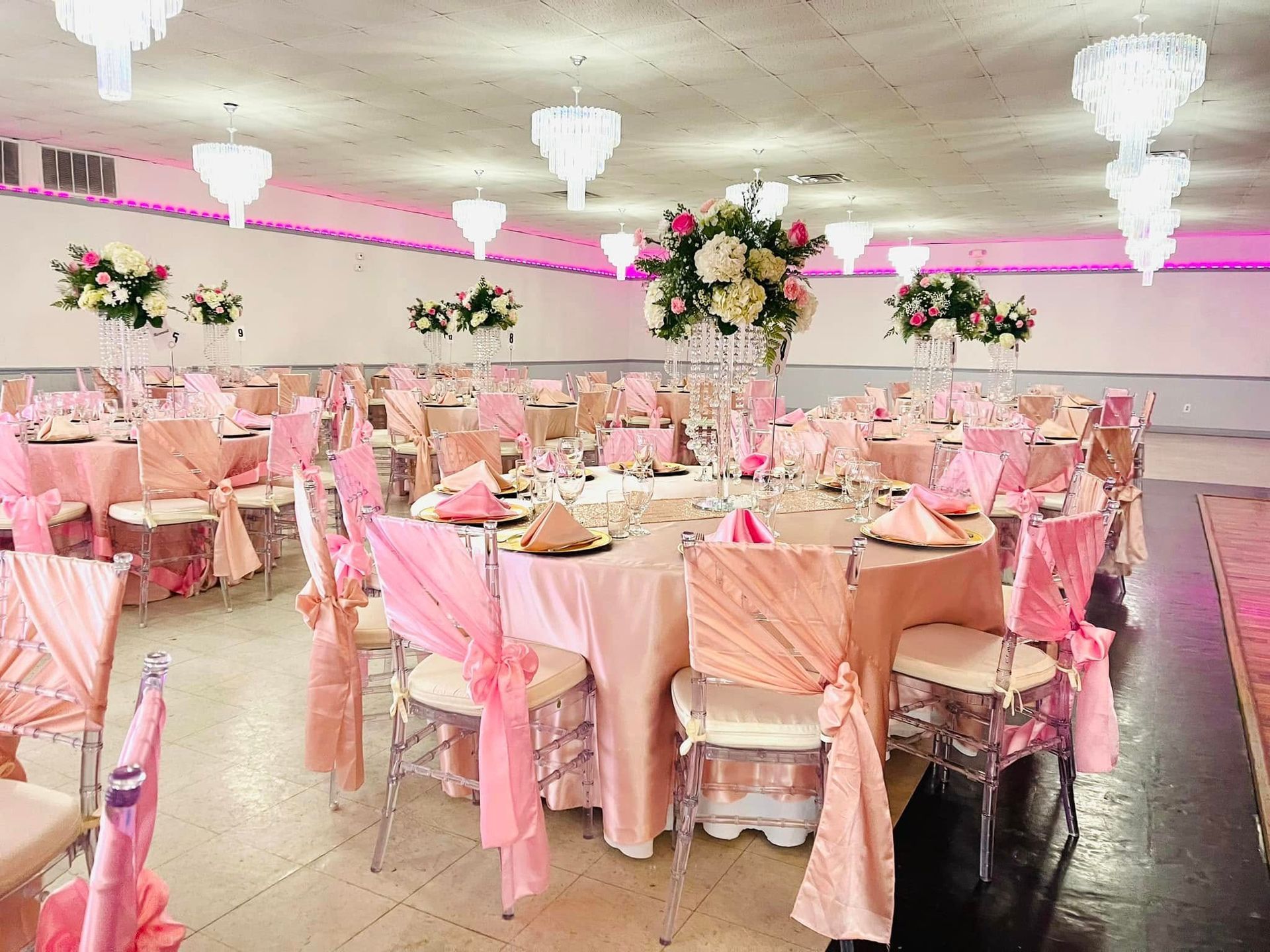 A large room filled with tables and chairs decorated in pink for a wedding reception.