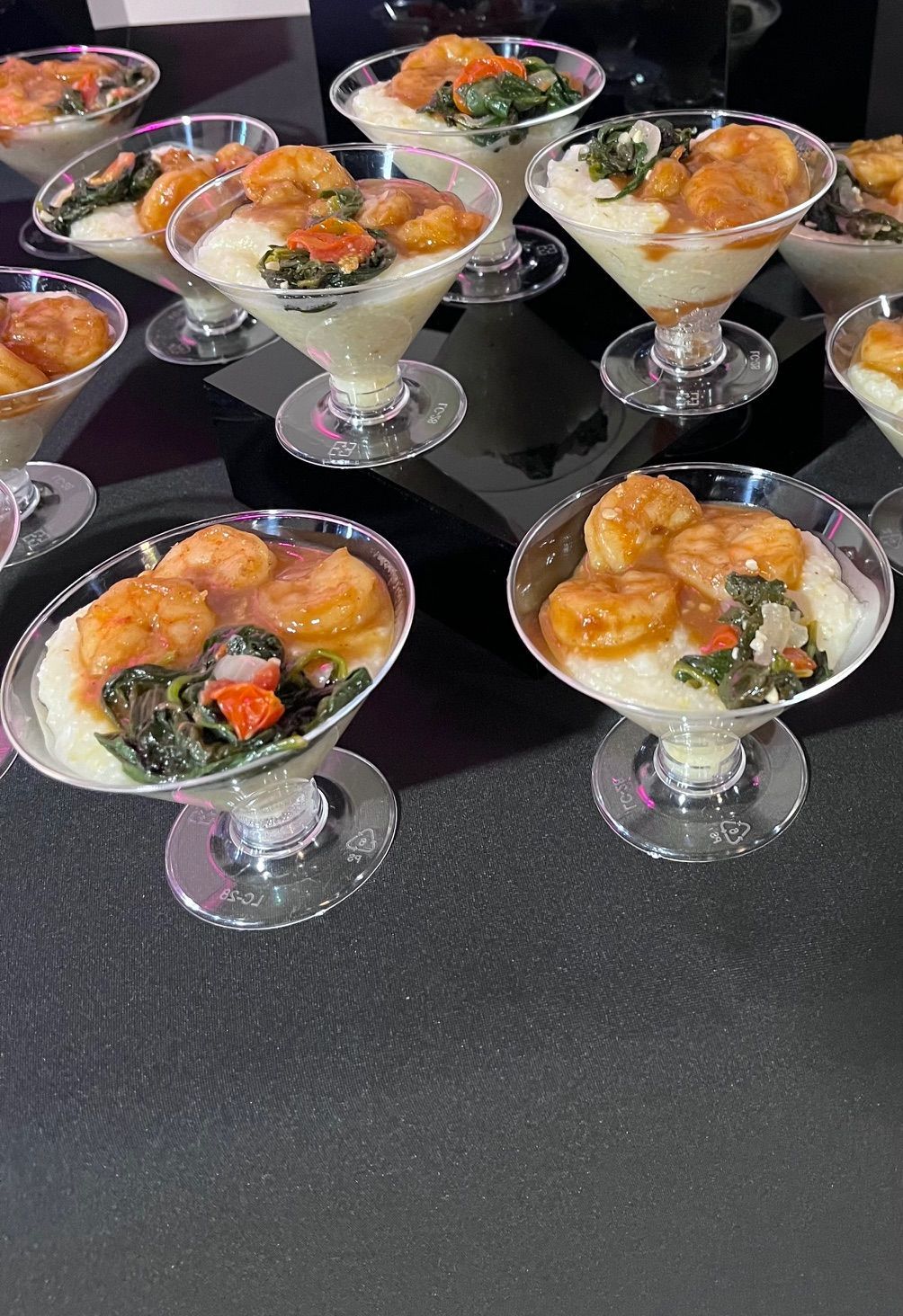 Shrimp and grits served in martini glasses on a black surface.