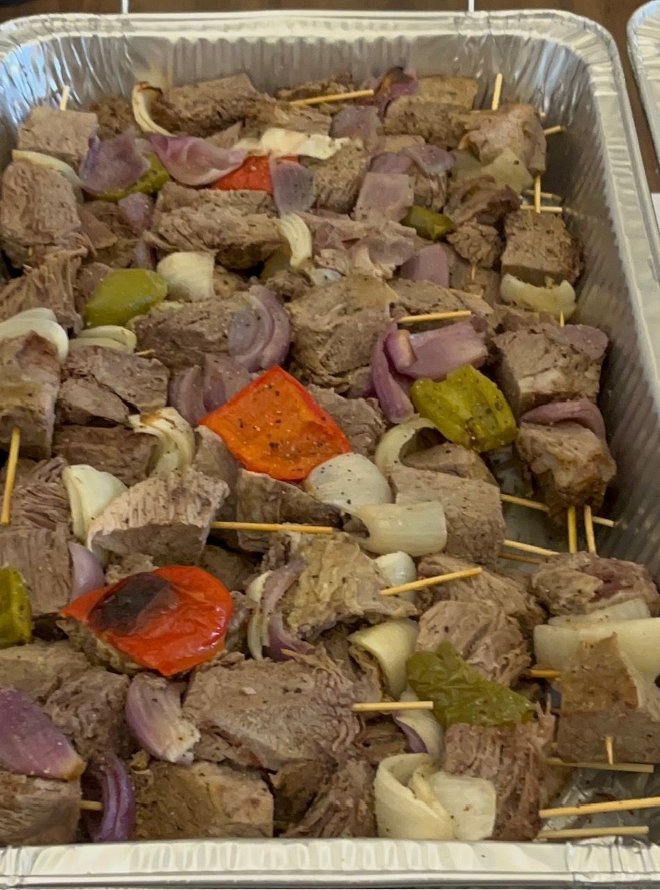 Kabobs on skewers in a silver pan; meat, red onion, red & green bell peppers.