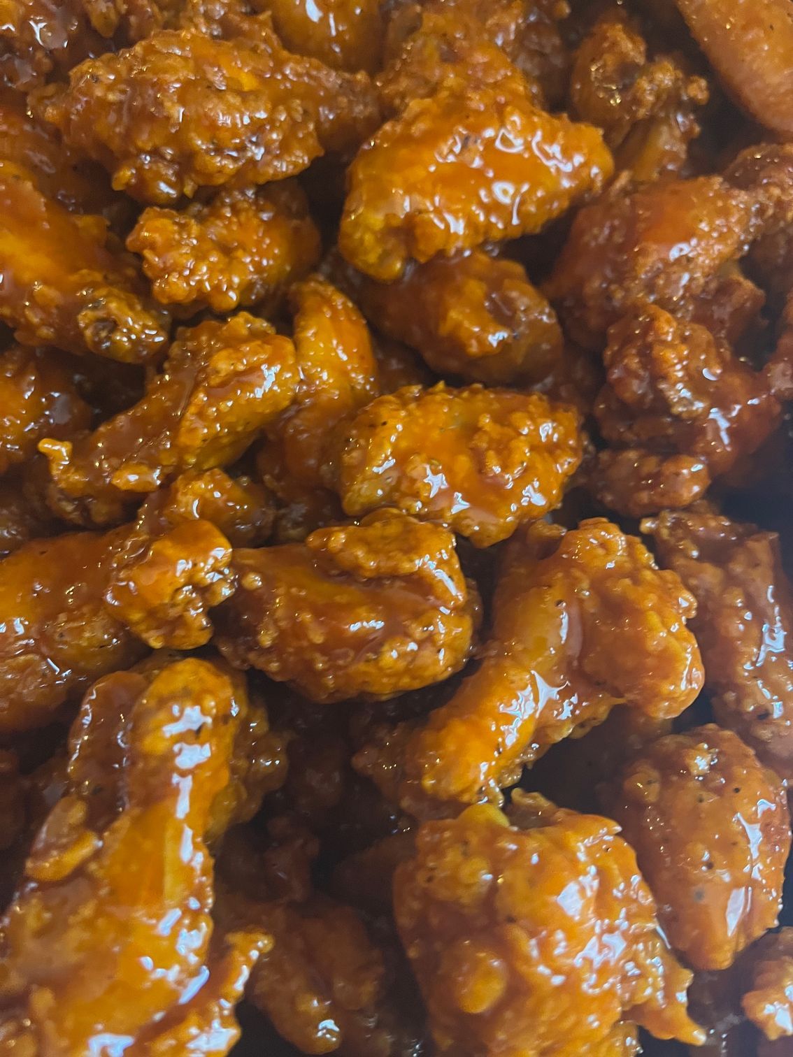 Pile of golden-brown, saucy chicken wings, close-up view.