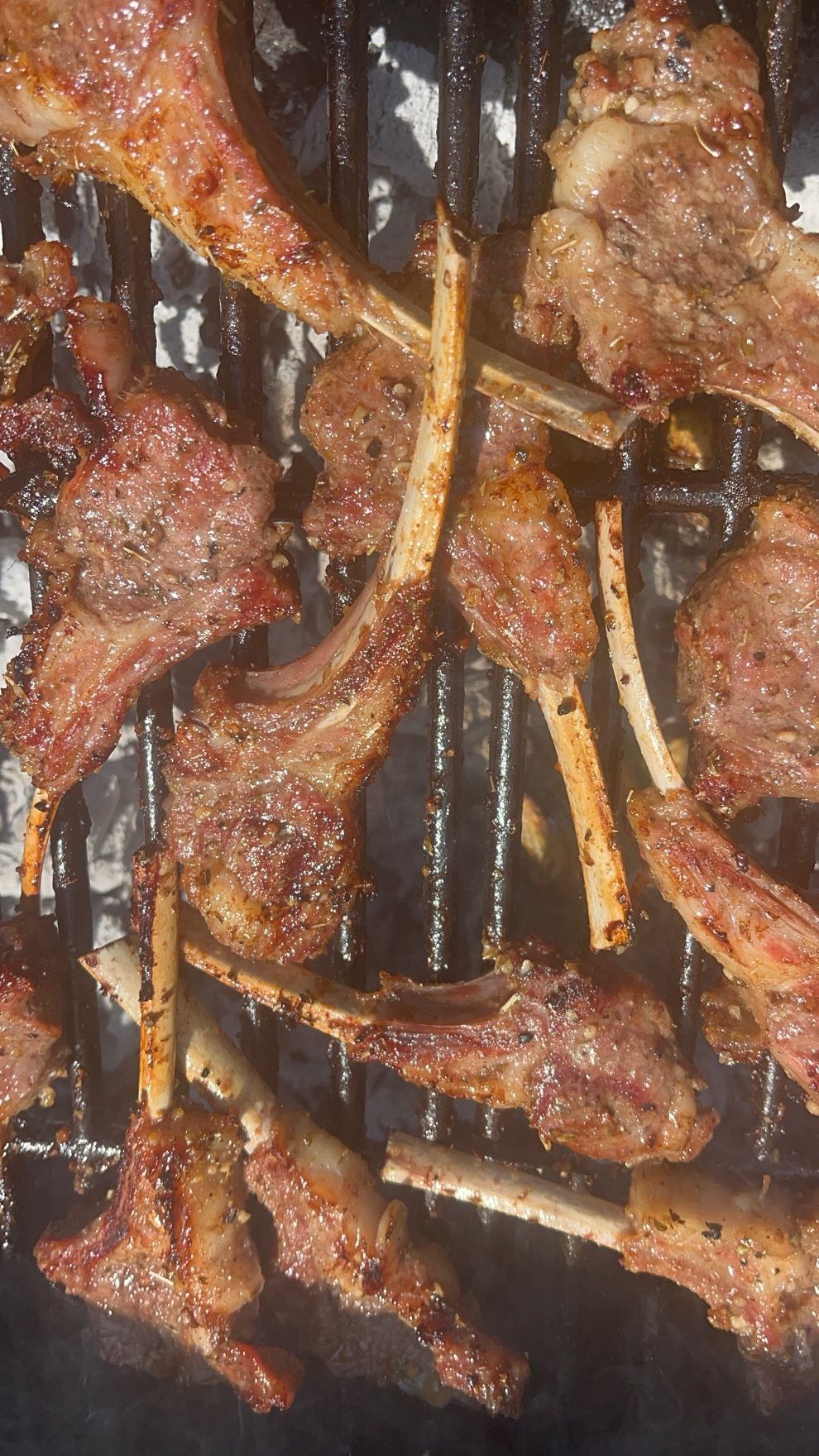 Grilled lamb chops on a grill, seasoned and seared with visible bones.