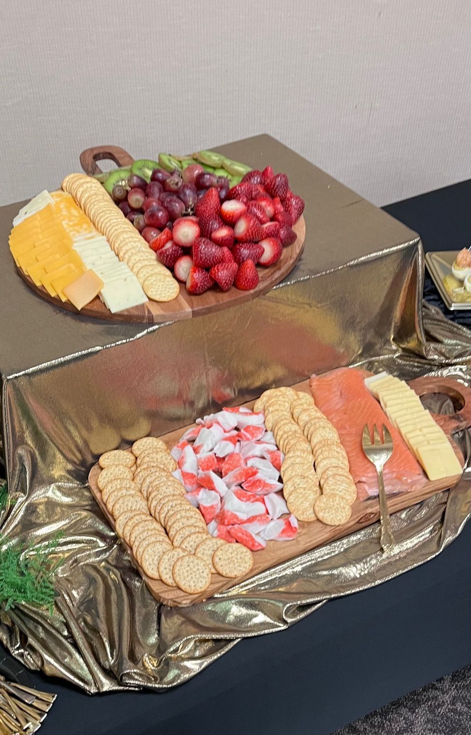 Two wooden platters of food. One with cheese, crackers and fruit. The other with crackers, imitation crab, salmon and cheese.
