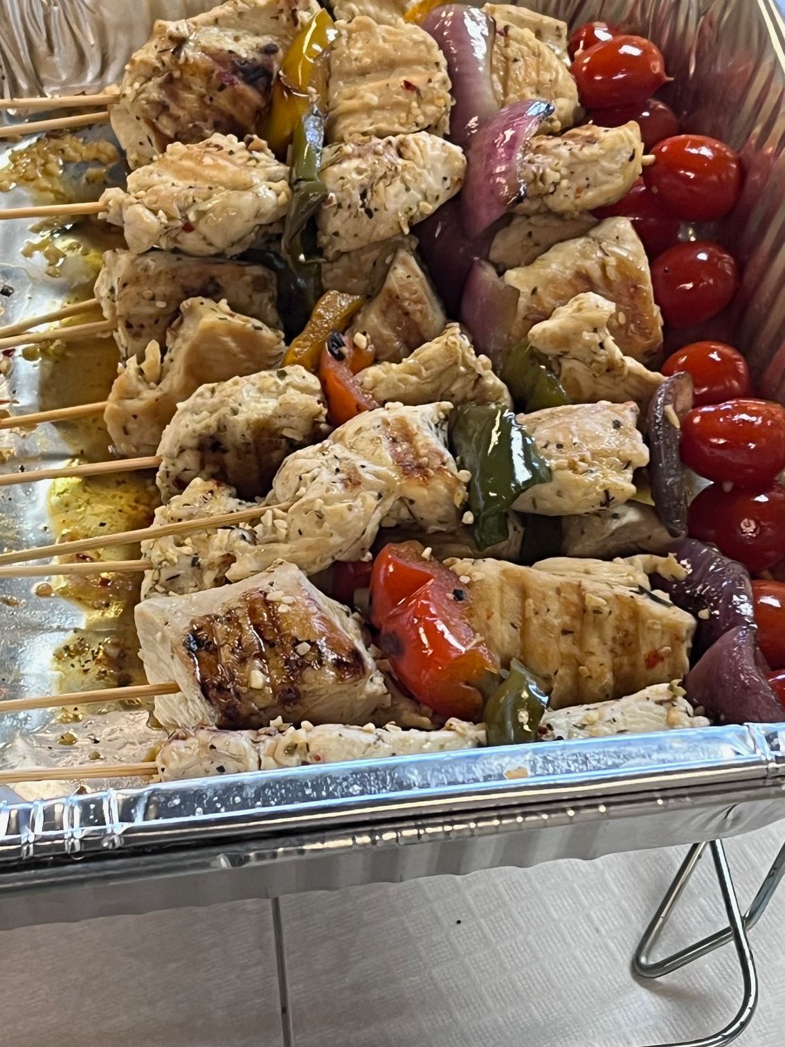 Chicken and vegetable skewers in a foil pan. Grilled chicken, bell peppers, red onion, and tomatoes.