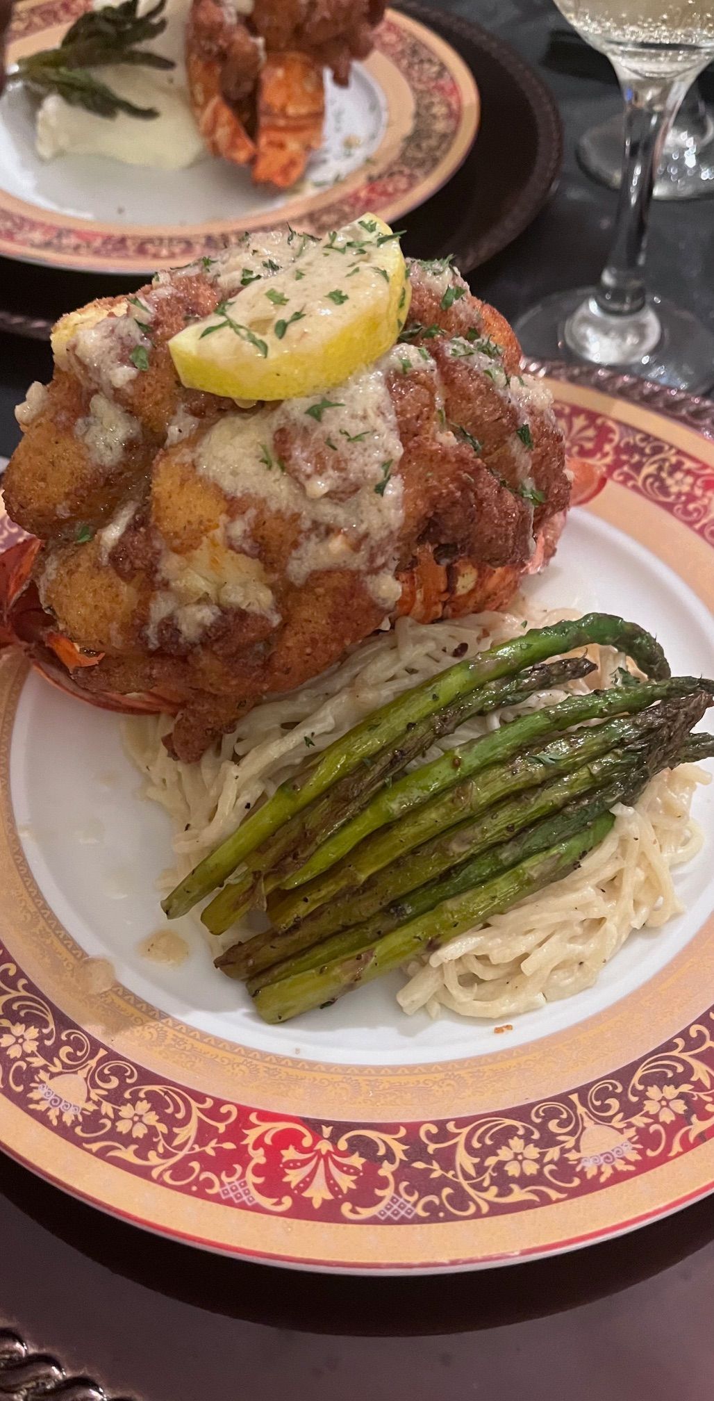 Lobster dish with fried topping, asparagus, and pasta on a decorative plate.