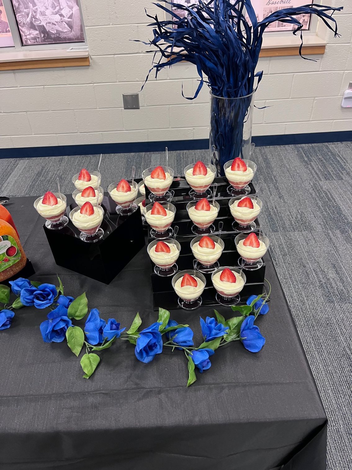 Dessert display: layered parfaits with strawberries, arranged on black risers, surrounded by blue floral accents.