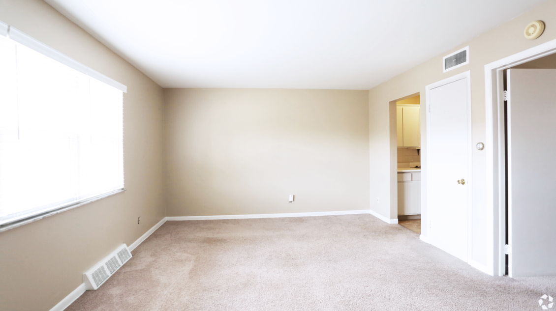 an empty living room with a carpeted floor and a refrigerator .