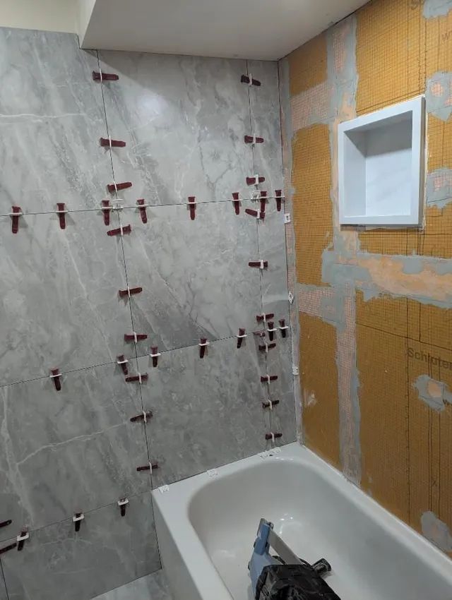 Bathroom under renovation with tiled shower wall, orange waterproofing, and a bathtub in the corner