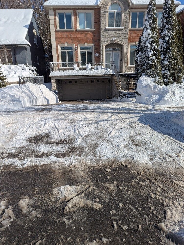 Snowy suburban townhouse with a driveway and garage, cleared path, and snow piled along the sides