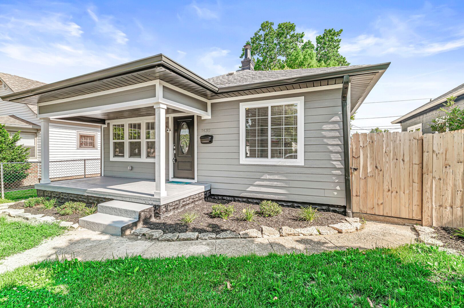 A small gray house with a wooden fence in front of it.