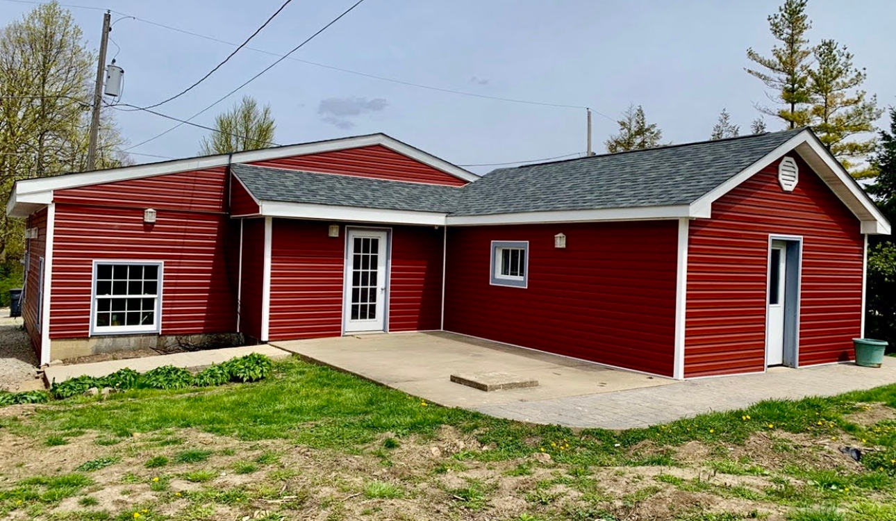 A red house with a gray roof is sitting in the middle of a grassy field.