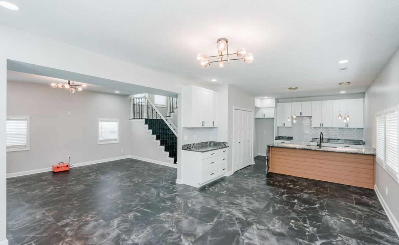 An empty living room with a kitchen and stairs in a house.