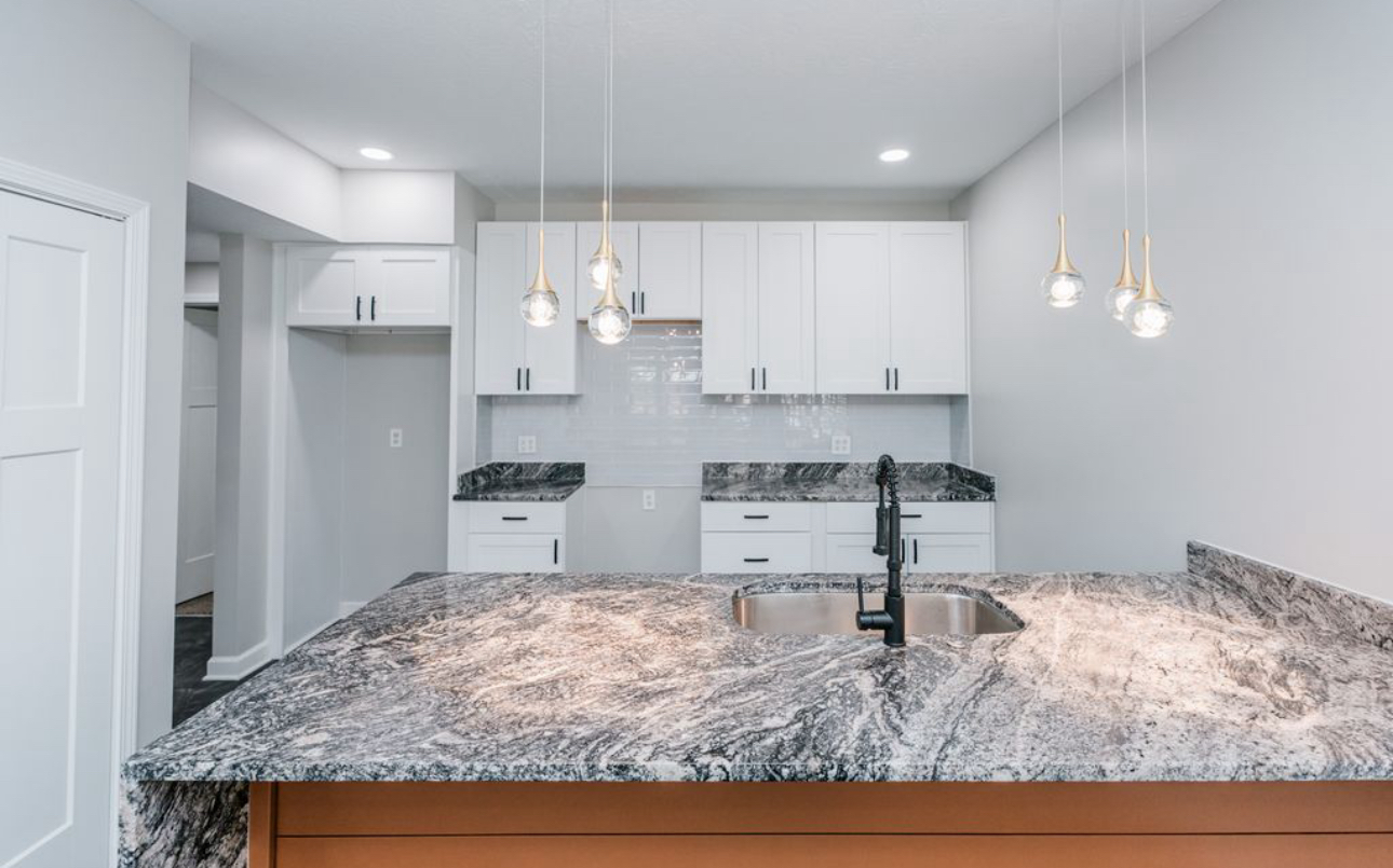 A kitchen with granite counter tops , white cabinets , and a sink.