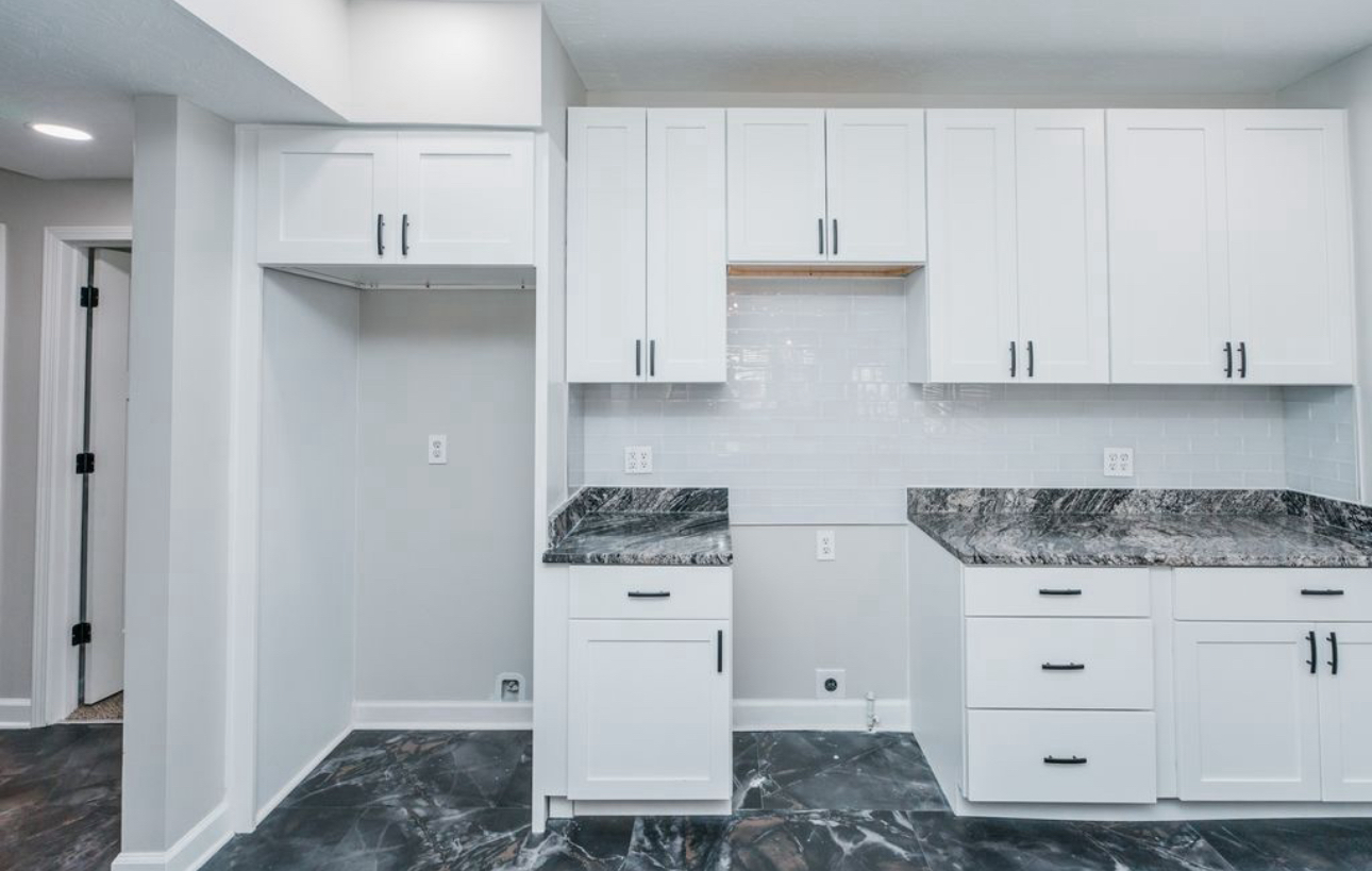 An empty kitchen with white cabinets and granite counter tops.