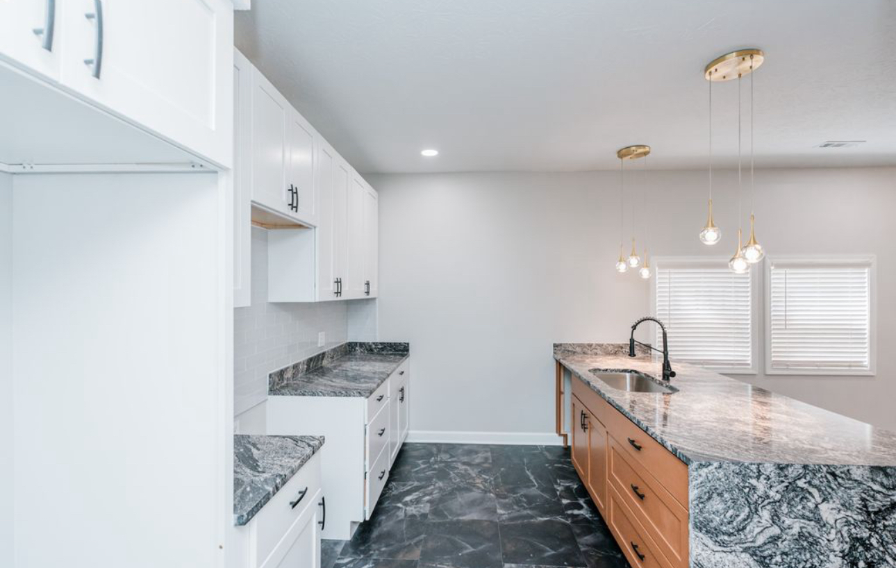 A kitchen with granite counter tops , white cabinets , and a large island.