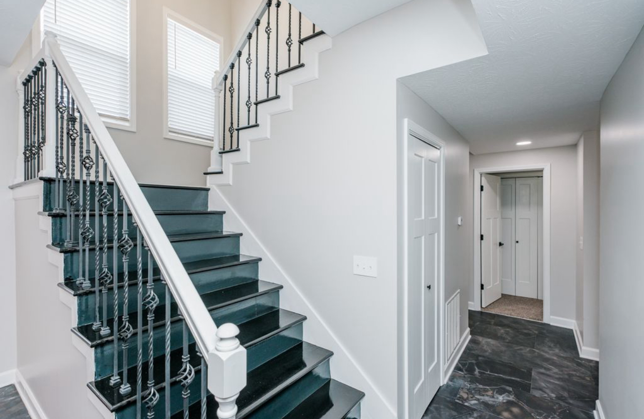 A staircase with black steps and a white railing in a hallway.