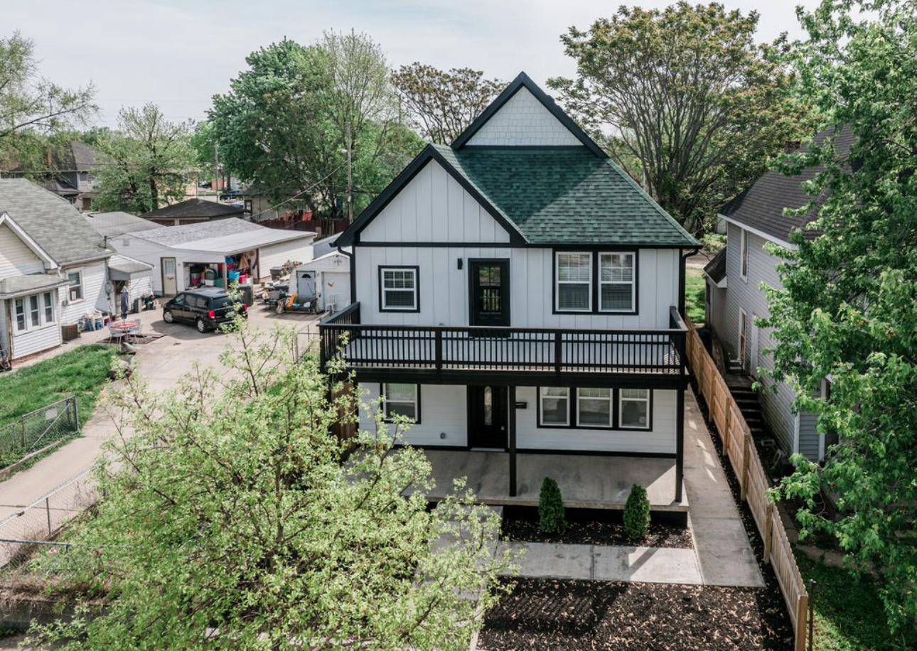An aerial view of a white house with a green roof