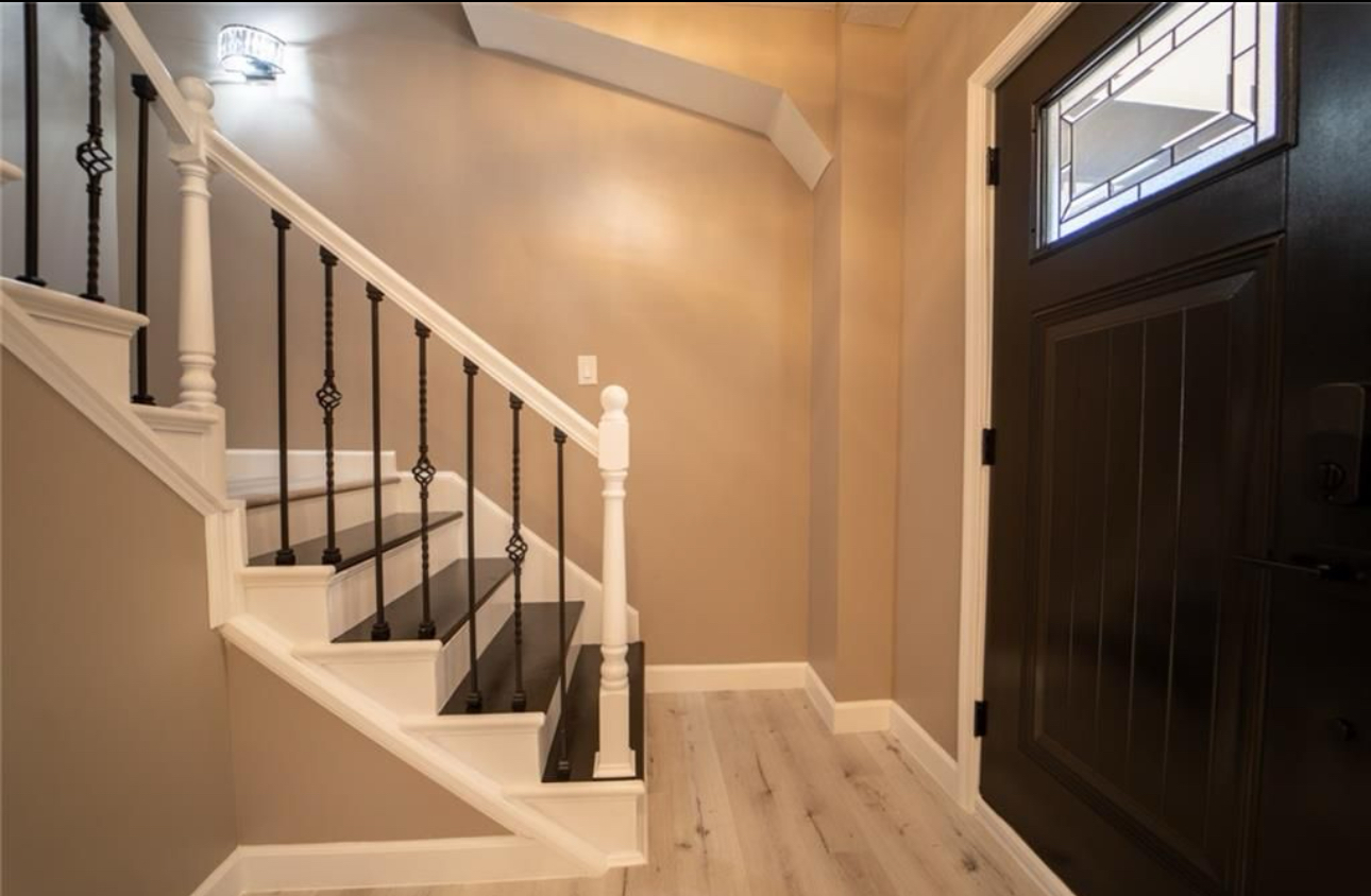 A hallway with stairs and a black door in a house.