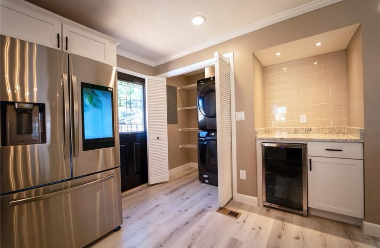 A kitchen with a refrigerator , washer and dryer , and a wine cooler.