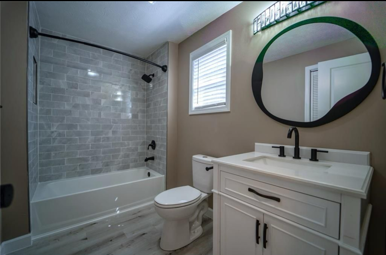 A bathroom with a toilet , sink , tub and mirror.