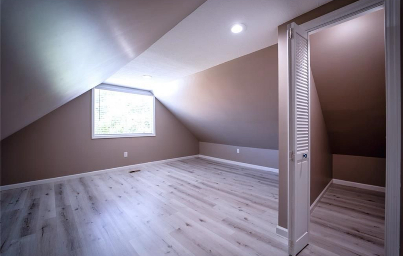 An empty attic with a window and hardwood floors.