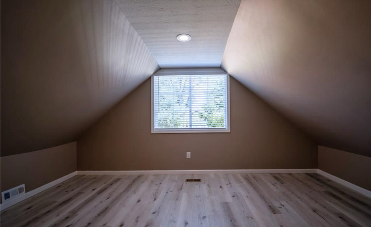 An empty attic with a window and hardwood floors.