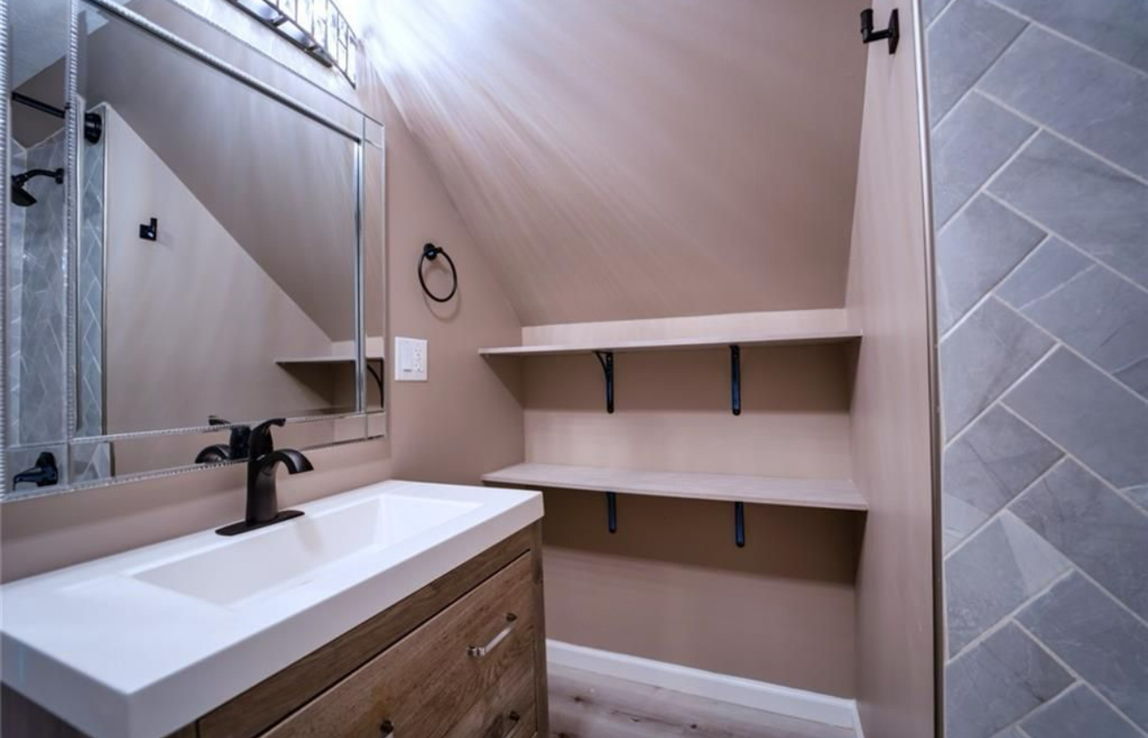 A bathroom with a sink , mirror and shelves.