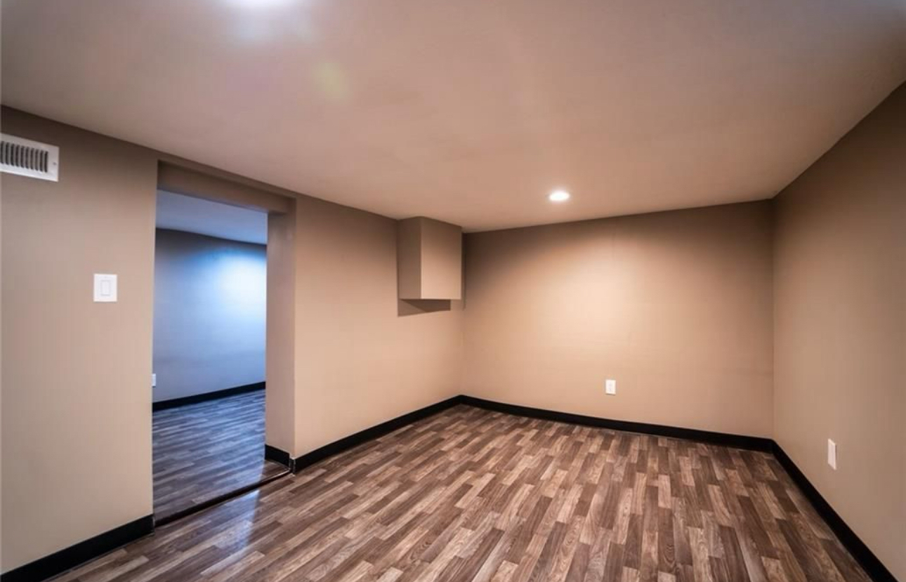 An empty room with a wooden floor and a door leading to another room.