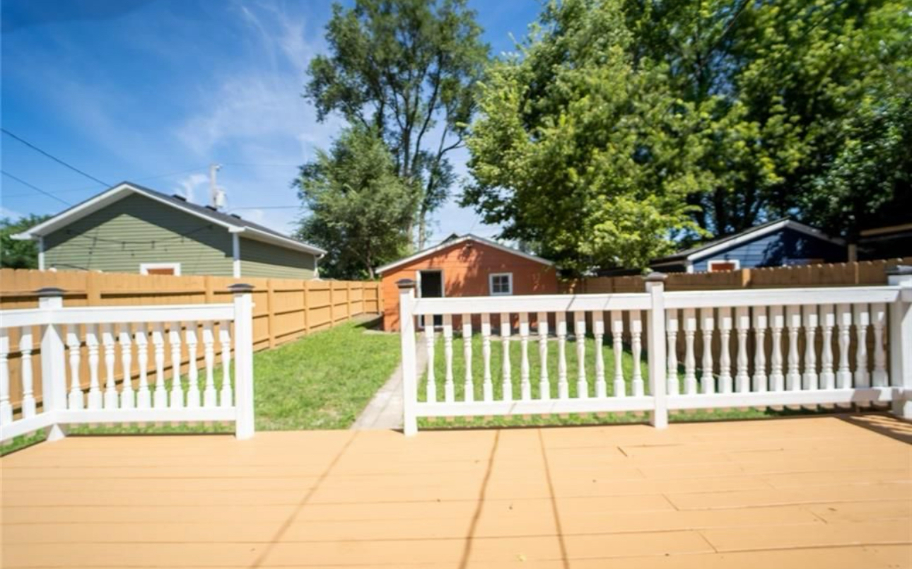 A white fence surrounds a backyard with a house in the background.