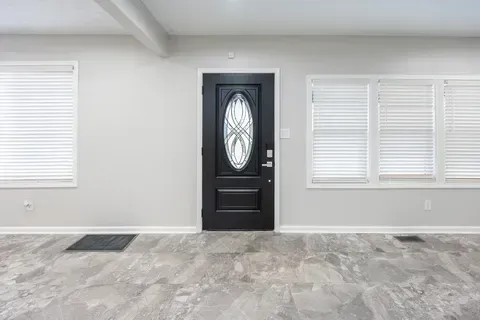An empty living room with a black door and white blinds.