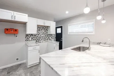 A kitchen with white cabinets , granite counter tops , a sink and a window.