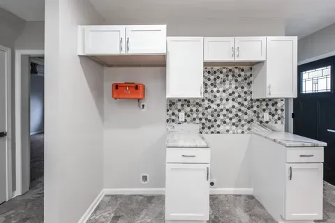 A kitchen with white cabinets and a black door.