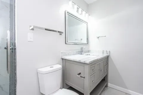 A bathroom with a toilet , sink , mirror and shower.