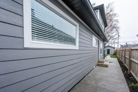 The side of a house with a concrete walkway and a wooden fence.