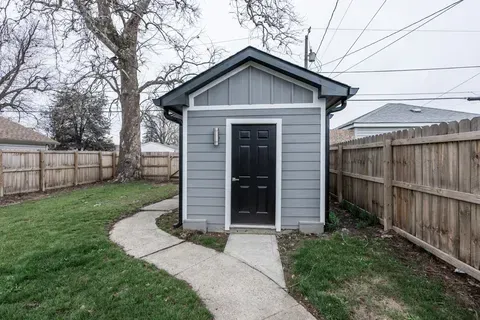 A small shed with a black door is in the backyard next to a wooden fence.