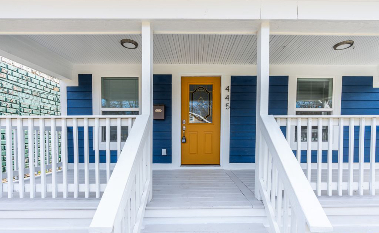 A blue house with a yellow door and a white porch.