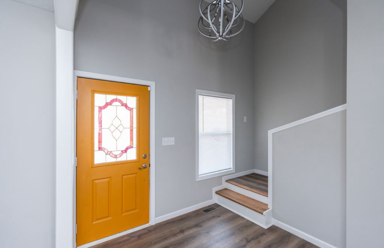 A hallway with a yellow door and stairs in a house.