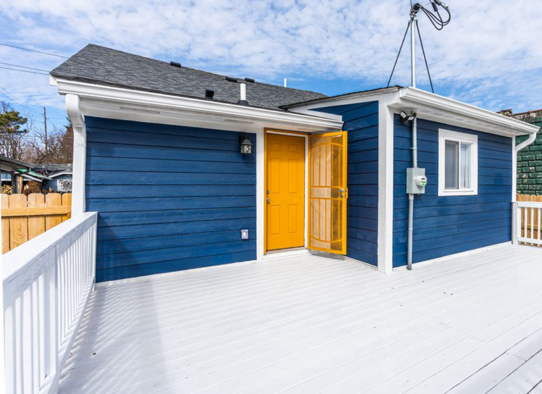 A blue house with a yellow door and a white deck.